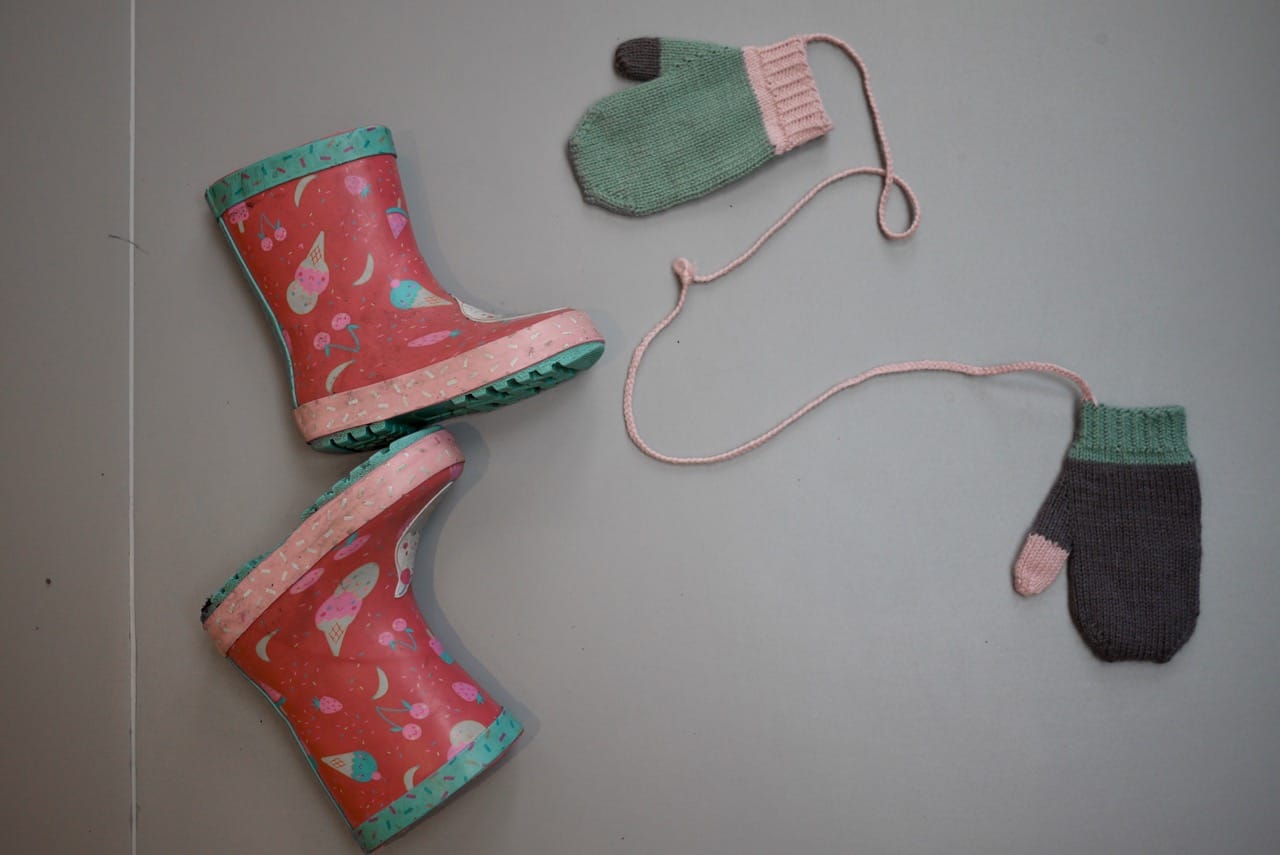 Pink, grey and green mittens attached with string with some wellies